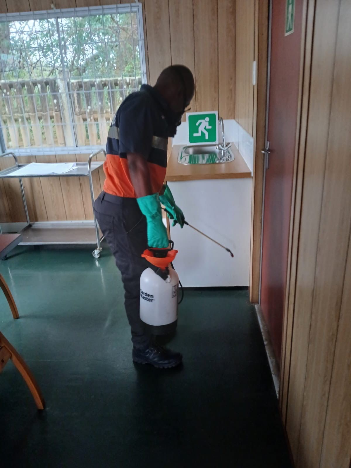 Pest Lab technician treating baseboard area in office kitchenette with pump sprayer